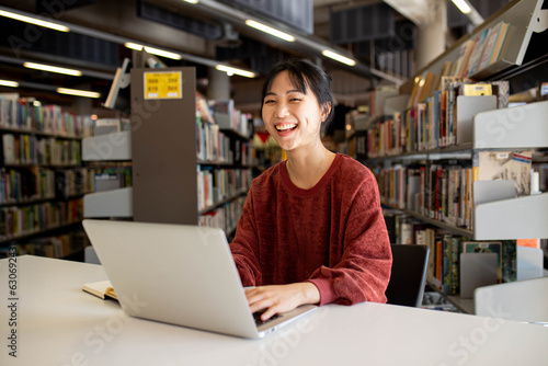 Young adult asian woman at the library studying and using her laptop photo