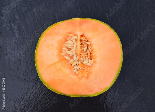 Obraz na plátne Half of ripe organic cantaloupe melon or muskmelon,
mushmelon, rockmelon on a black stone background