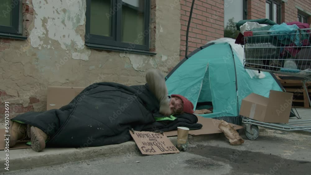 Medium long view of poor tramp sleeping on street next to self-made ...