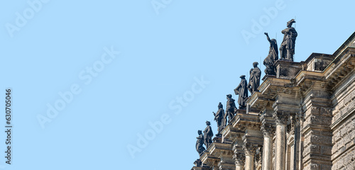 Old roof statutes of high ranked priests  saints  artists  phylosophers lined up in the city opera building in downtown of Dresden  Germany  details  at blue sky solid background with copy space.