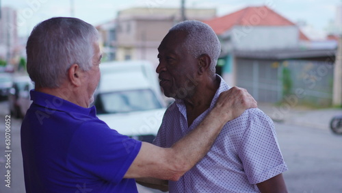 Two elderly diverse friends exchange hug in urban setting. African American male embracing his caucasian friend depicting a scene of friendship and camaraderie in street
