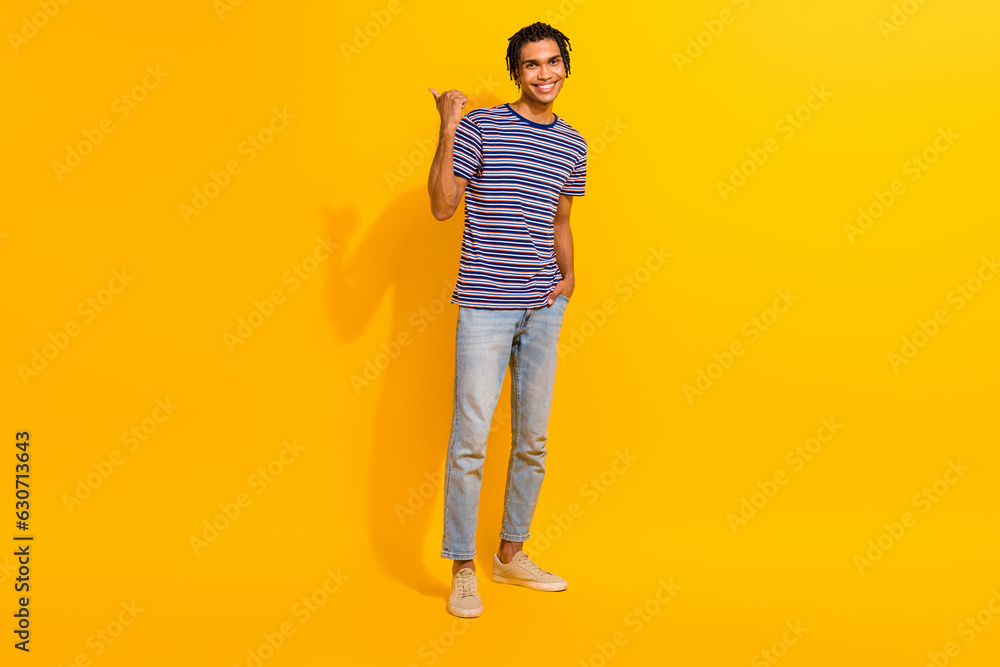 Full size photo of satisfied man dressed striped t-shirt directing at promo empty space arm in pocket isolated on yellow color background Full size photo of satisfied man dressed striped t-shirt directing at promo empty space arm in pocket isolated on yellow color background