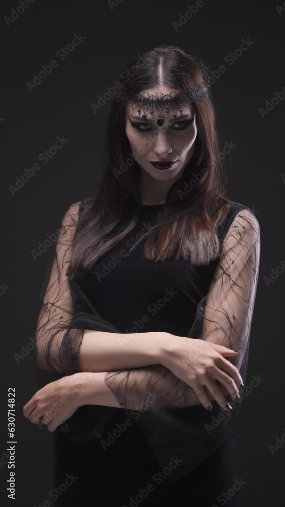 Mystical woman in black attire looking at the camera, halloween feast of all saints, portrait of a beautiful young woman, vertical video. Mystical woman in black attire looking at the camera, halloween feast of all saints, portrait of a beautiful young woman, vertical video.