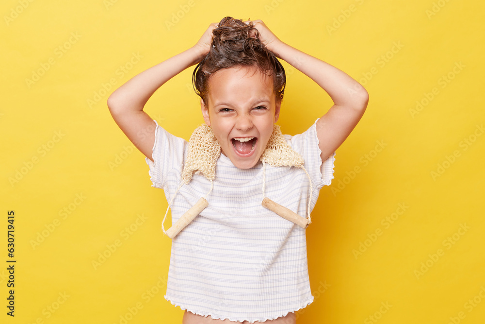 Excited crazy little girl with wet hair wearing casual white T-shirt standing isolated over yellow background washing hair screaming with widely open mouth Excited crazy little girl with wet hair wearing casual white T-shirt standing isolated over yellow background washing hair screaming with widely open mouth