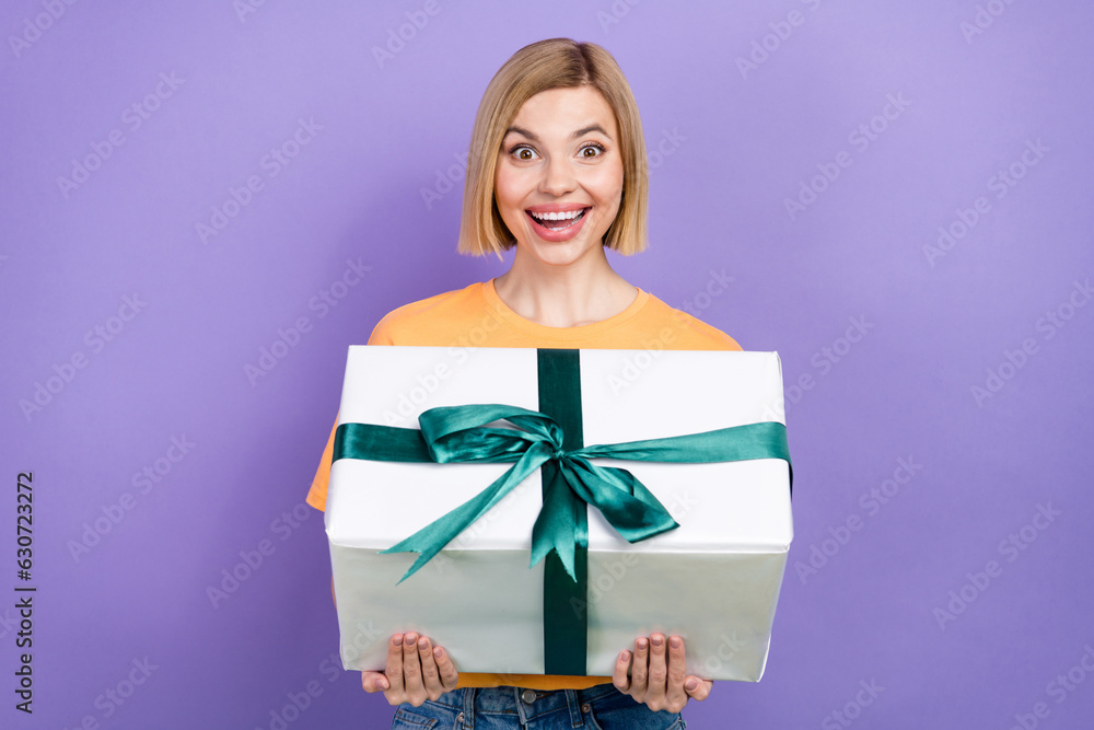 Photo of impressed woman with bob hairstyle wear yellow t-shirt hold present box staring open mouth isolated on purple color background Photo of impressed woman with bob hairstyle wear yellow t-shirt hold present box staring open mouth isolated on purple color background