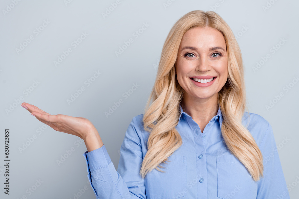 Photo of cheerful blond woman holding open palm showing empty space product wear blue shirt isolated grey color background Photo of cheerful blond woman holding open palm showing empty space product wear blue shirt isolated grey color background