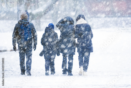 Family walks down the street in winter in a strong snowstorm, winter snowstorm, bad weather