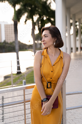 Young woman in yellow dress standing near water in city park