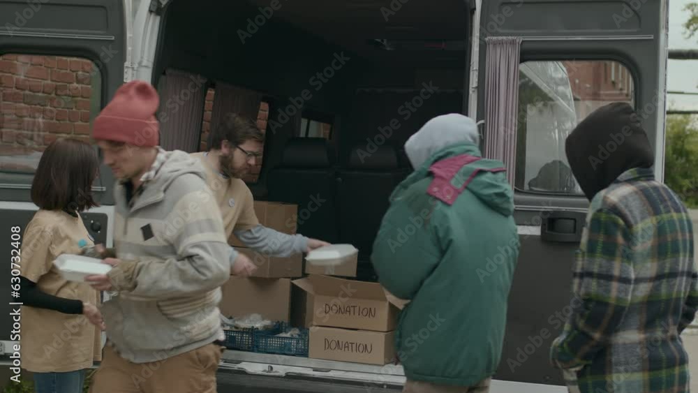 Medium long shot of volunteers giving free food and water to people in need at daylight Medium long shot of volunteers giving free food and water to people in need at daylight