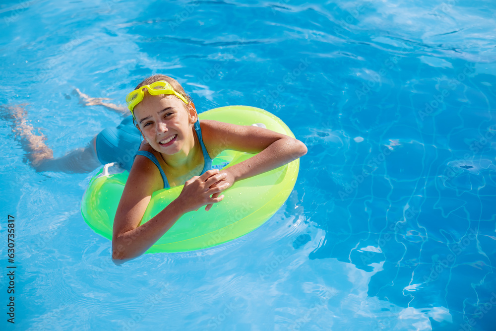 Smiling cute teenage girl wearing swimming glasses and a large swimming circle in the pool on a sunny summer day.