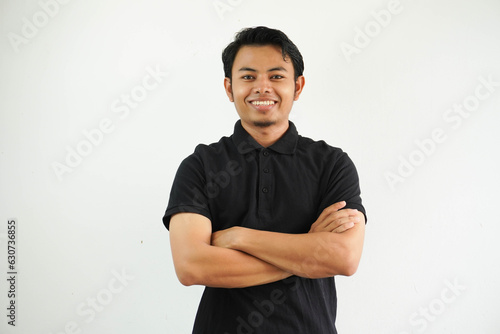 young asian man smiling happy at the camera with arms crossed wearing black polo t shirt isolated on white background