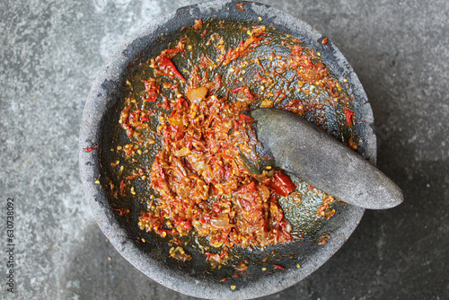Sambal is an Indonesian chilli sauce or paste, made from red chili pepper and onion, mashed by stone mortar and pestle. Flat lay, top view or overhead view photo