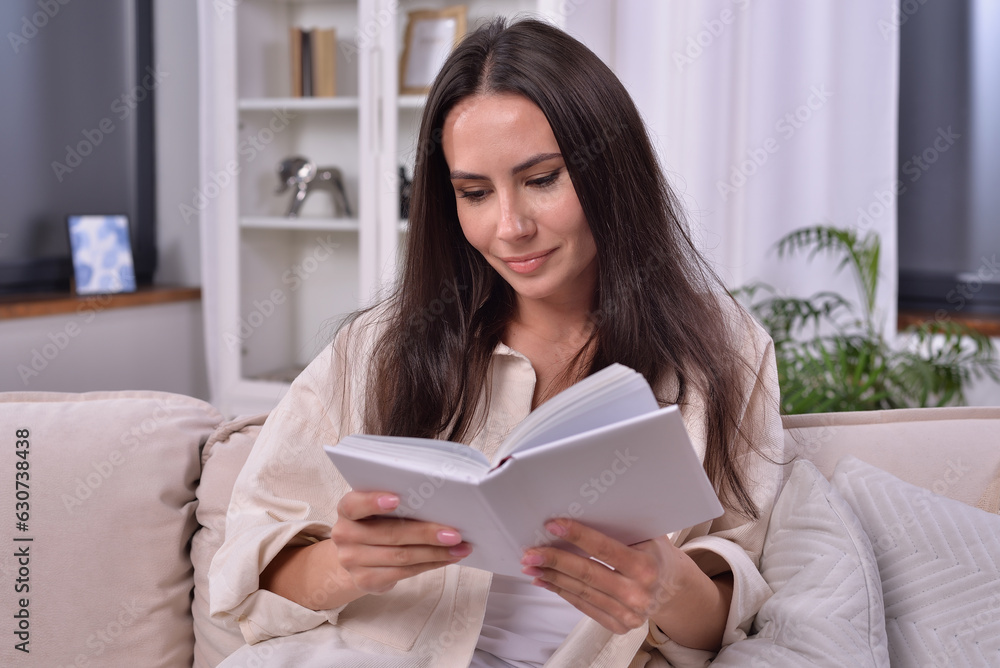 Relaxed woman indulged in reading a captivating book on a cozy sofa. She is engrossed in the story, with a peaceful expression on her face. A perfect moment of leisure and relaxation. Relaxed woman indulged in reading a captivating book on a cozy sofa. She is engrossed in the story, with a peaceful expression on her face. A perfect moment of leisure and relaxation.