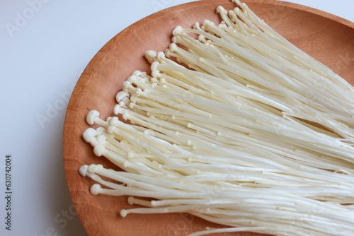 Enoki mushroom, or enokitake or Flammulina filiformis, on wooden plate, isolated on white background photo