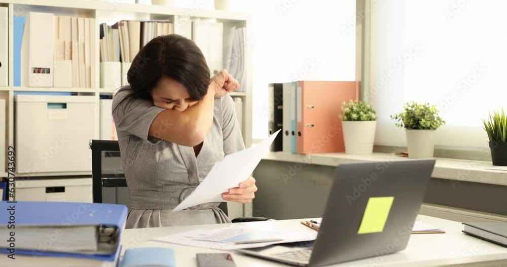 Young woman working at workplace sneezes violently. Respiratory infections seasonality and business concept Young woman working at workplace sneezes violently. Respiratory infections seasonality and business concept