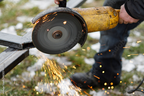 Close up of man grinding metal with circular grinder disc and electric sparks. Worker cutting metal with angle grinder for welding. Workers making fence with shielded metal arc welding photo