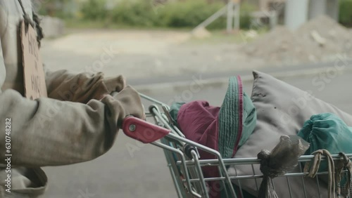 Cropped shot of man walking along road with things in shopping cart in unknown direction