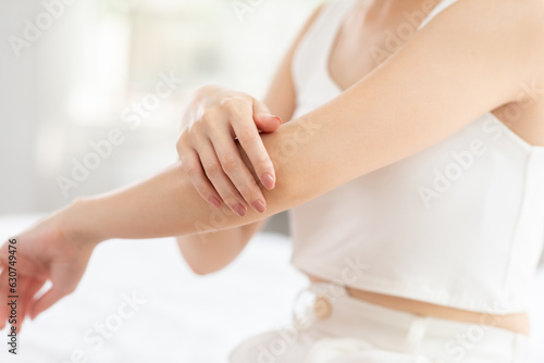 Beautiful Asian young woman apply cream or lotion on her arm for protect dry skin for moisturizing on skin. Healthy skin of young female doing self care at home. Woman self care concept