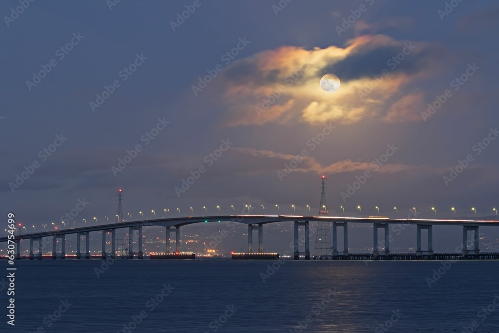 a long bridge going over the ocean with a moon shining Moonrise over Bridge, San Francisco Bay Area
