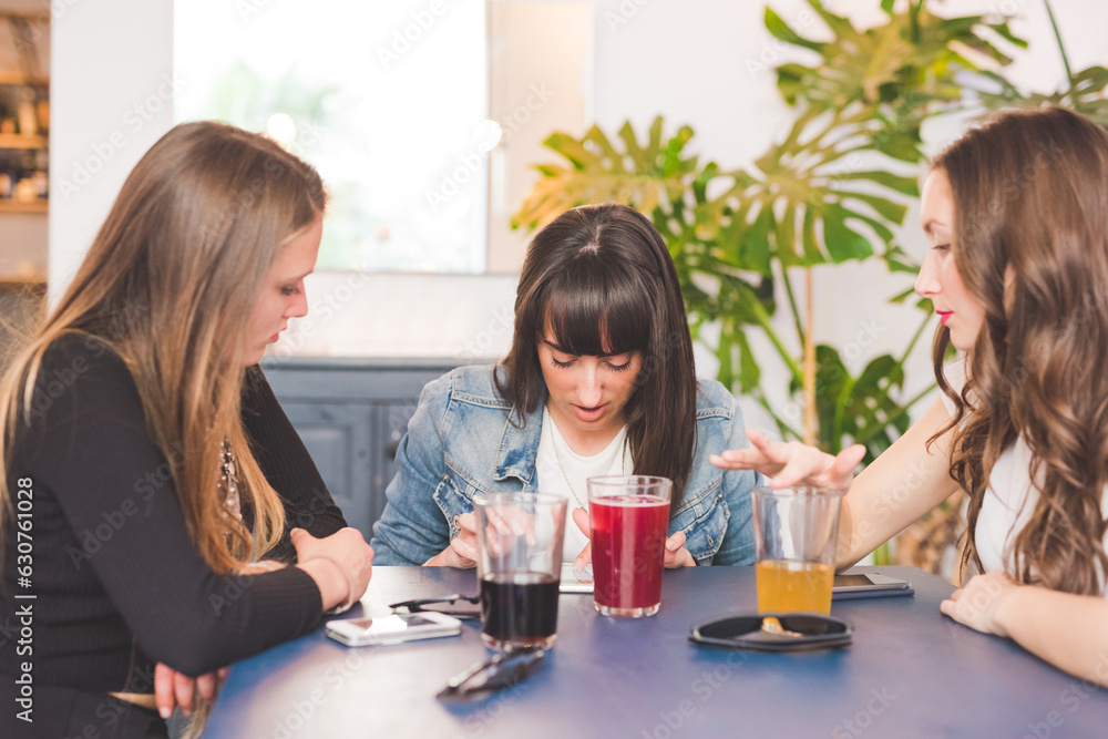 Three young women sitting indoors bar chatting using smartphone drinking soft drink Three young women sitting indoors bar chatting using smartphone drinking soft drink