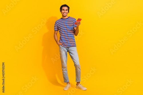 Full length photo of nice positive person hold use smart phone chatting empty space isolated on yellow color background
