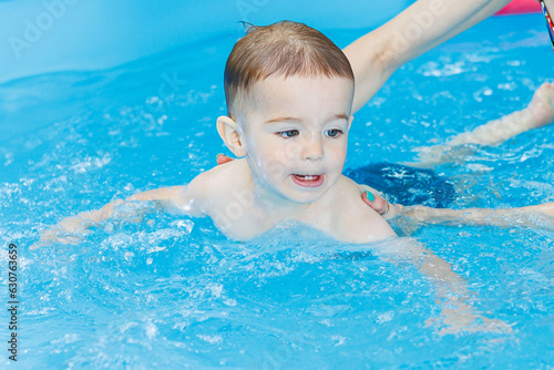 A 2-year-old boy learns to swim in a pool with a coach. Swimming lessons for children. Swimming school for children. Educational swimming courses for children