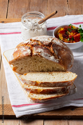 Round yeast bread made from white and whole grain flour, tomato salad and pate on a wooden background. Rustic style.