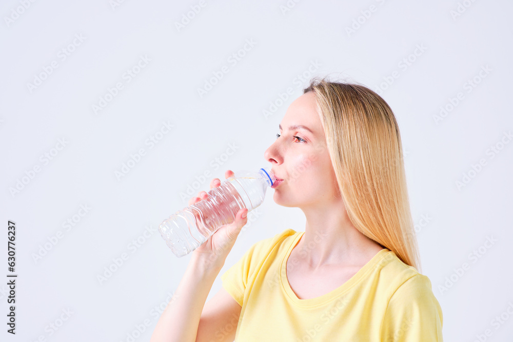 young blonde girl with drinking water from a plastic bottle in yellow t-shirt on a white background young blonde girl with drinking water from a plastic bottle in yellow t-shirt on a white background
