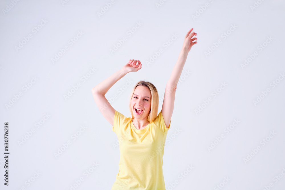 cheerful young blonde girl celebrating with arms up in yellow t-shirt on white background cheerful young blonde girl celebrating with arms up in yellow t-shirt on white background
