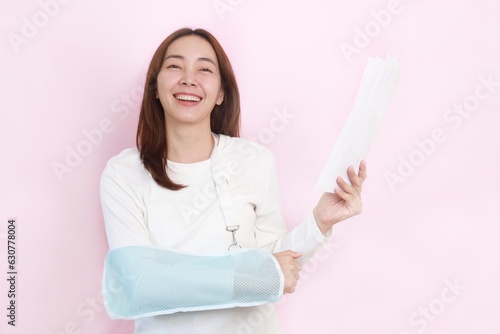 
Patient with broken arm in sling, Asian woman in casual white shirt broken hand wearing an arm brace standing over pink background with copy space.