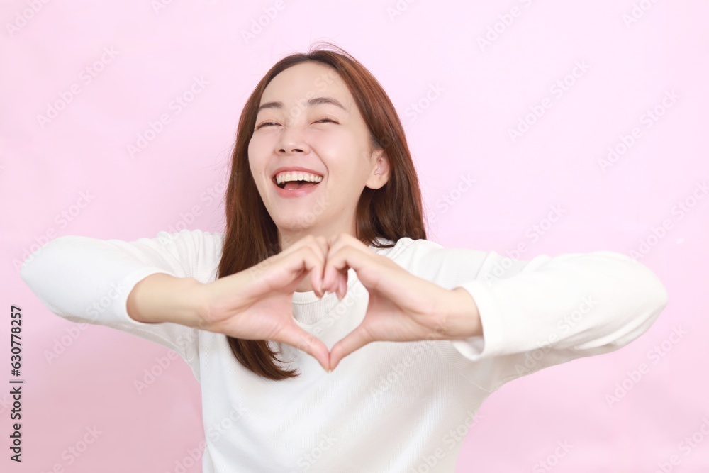 Beautiful Asian woman making hands shape of heart over pink background with copy space. Beautiful Asian woman making hands shape of heart over pink background with copy space.