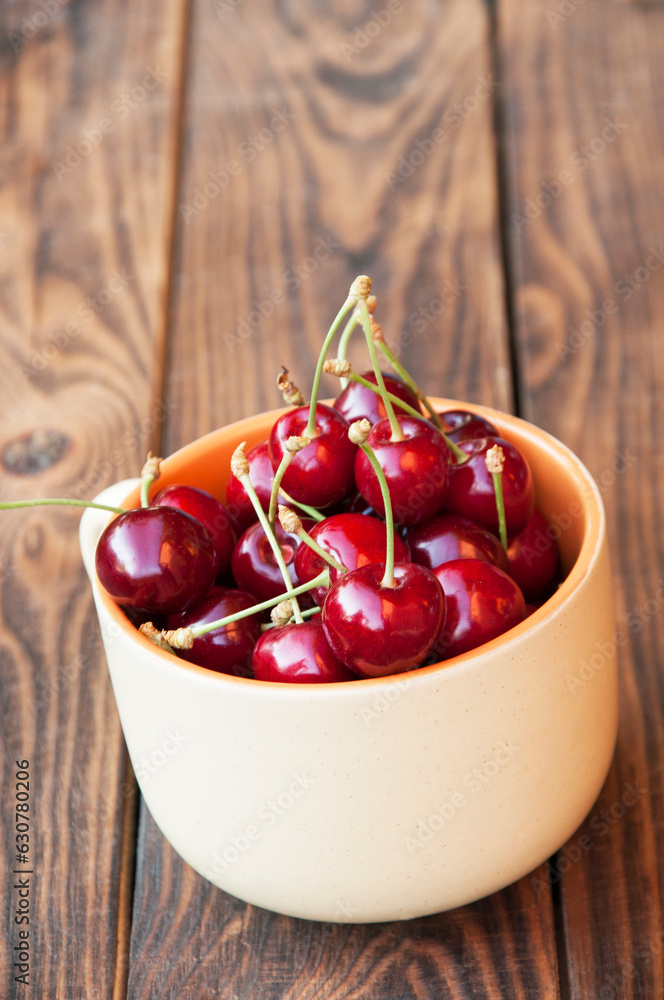 ripe red cherries in a white cup on a wooden background. a lot of sweet cherries on a brown table.the concept of making cherry jam ripe red cherries in a white cup on a wooden background. a lot of sweet cherries on a brown table.the concept of making cherry jam