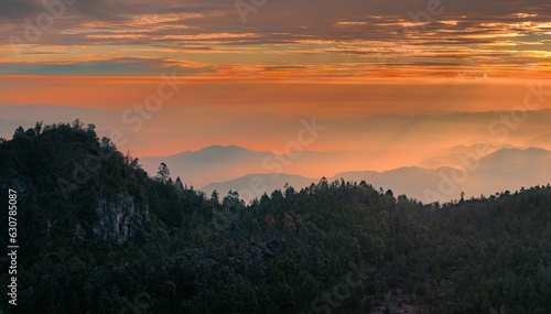 a sky filled with a very orange sunset behind mountains and trees