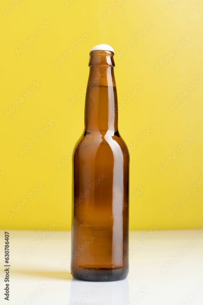 Brown beer bottle standing on a white table against a yellow background Brown beer bottle standing on a white table against a yellow background