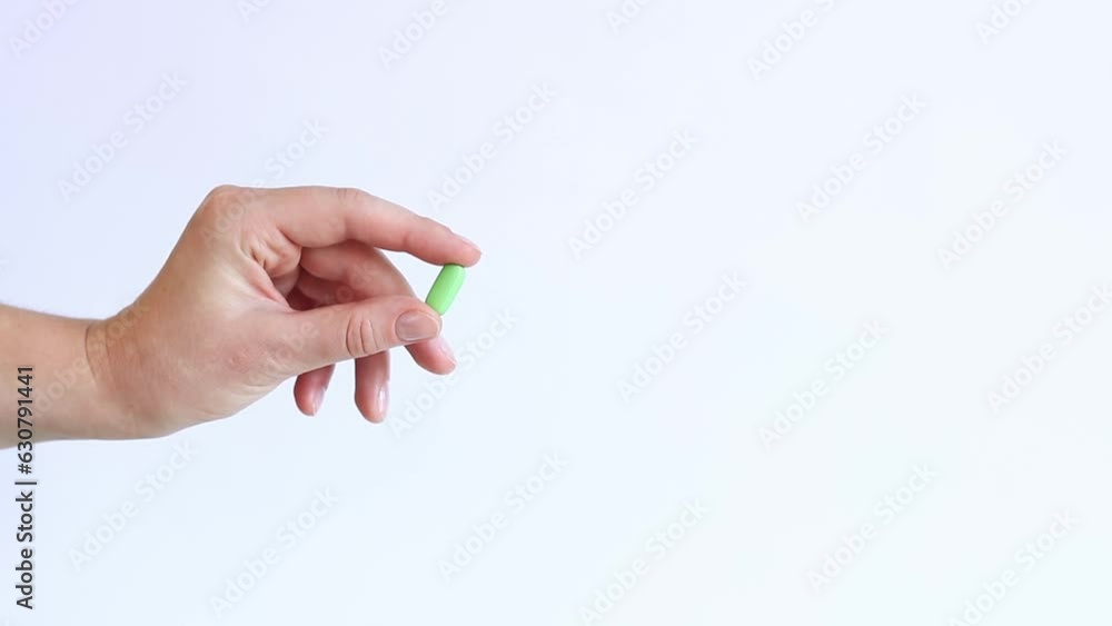 Vitamins on a white background. The hand holds one green pill with two fingers. The concept of medicine and health. Vitamins and dietary supplements Vitamins on a white background. The hand holds one green pill with two fingers. The concept of medicine and health. Vitamins and dietary supplements