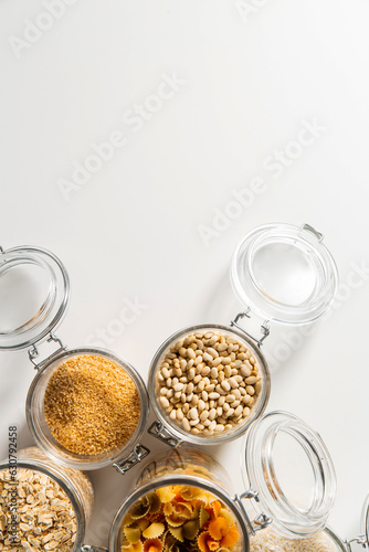 food storage, culinary and eating concept - close up of jars with different cereals, pasta and beans on white background, top view