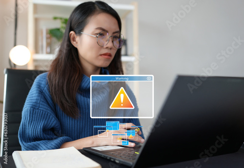 Asian woman using laptop feeling worried of problem message, risk alert symbol while accessing computer device through internet network. Data security protection systems are attacked by cyber threats.