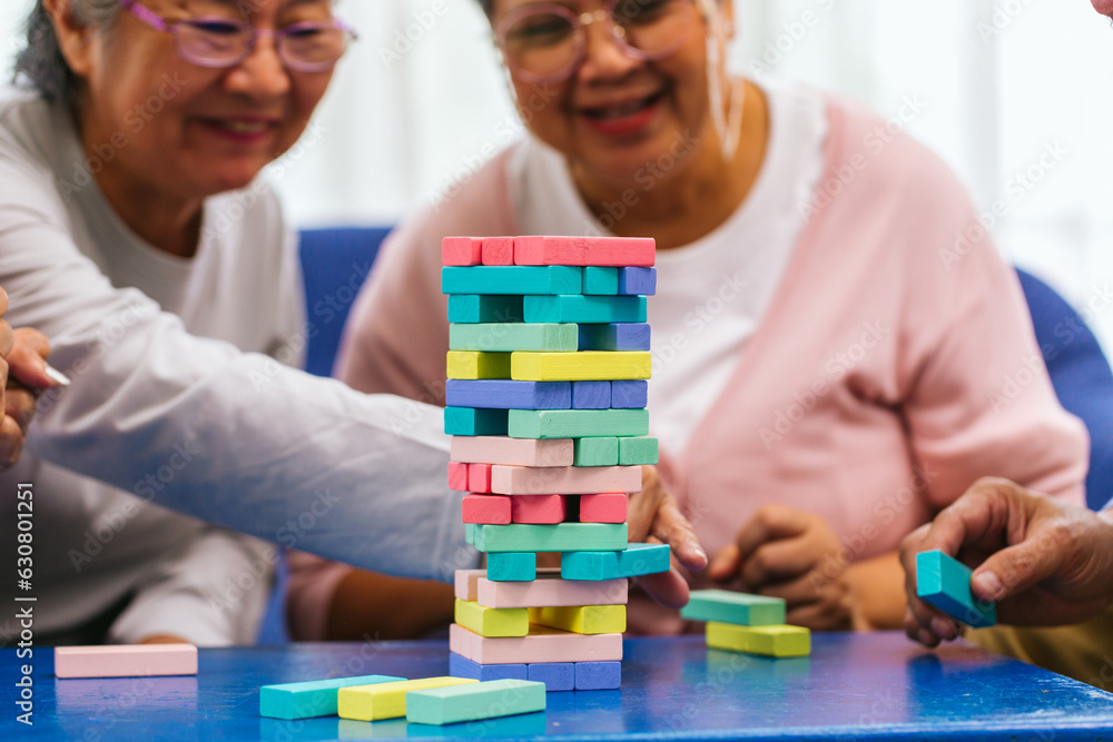 Senior people playing a wooden block tower, risk and strategy of project management. Concept of business risk with domino blocks. Older People playing jenga block removal game on table at home Senior people playing a wooden block tower, risk and strategy of project management. Concept of business risk with domino blocks. Older People playing jenga block removal game on table at home