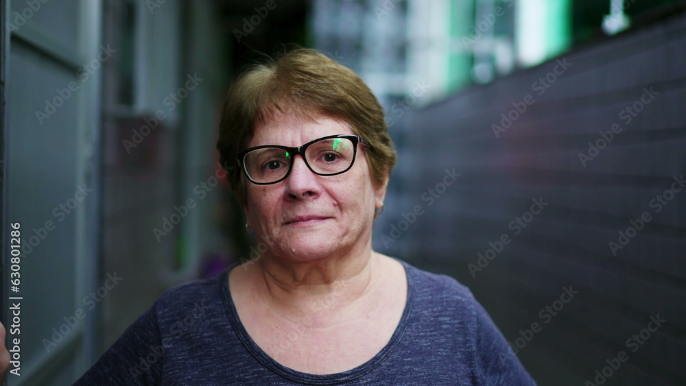 Obraz premium Portrait of a serious elderly woman looking at camera standing in residential corridor in Brazil. Close-up face of a stern senior lady