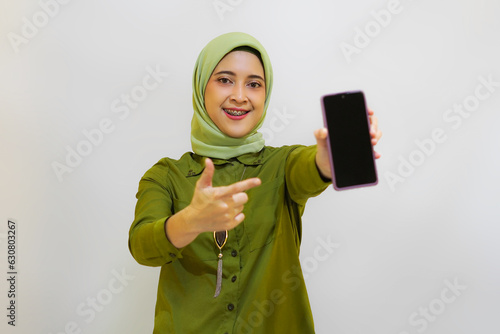 Happy Young Asian woman holding her phone for advertising concept. Green outfit hijab woman concept photo