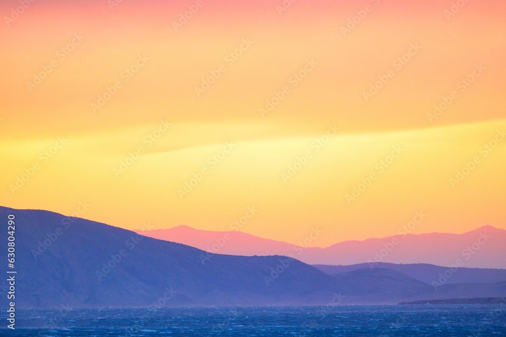 Scenic view of a stunning sunset over the ocean, with colorful mountains in the background