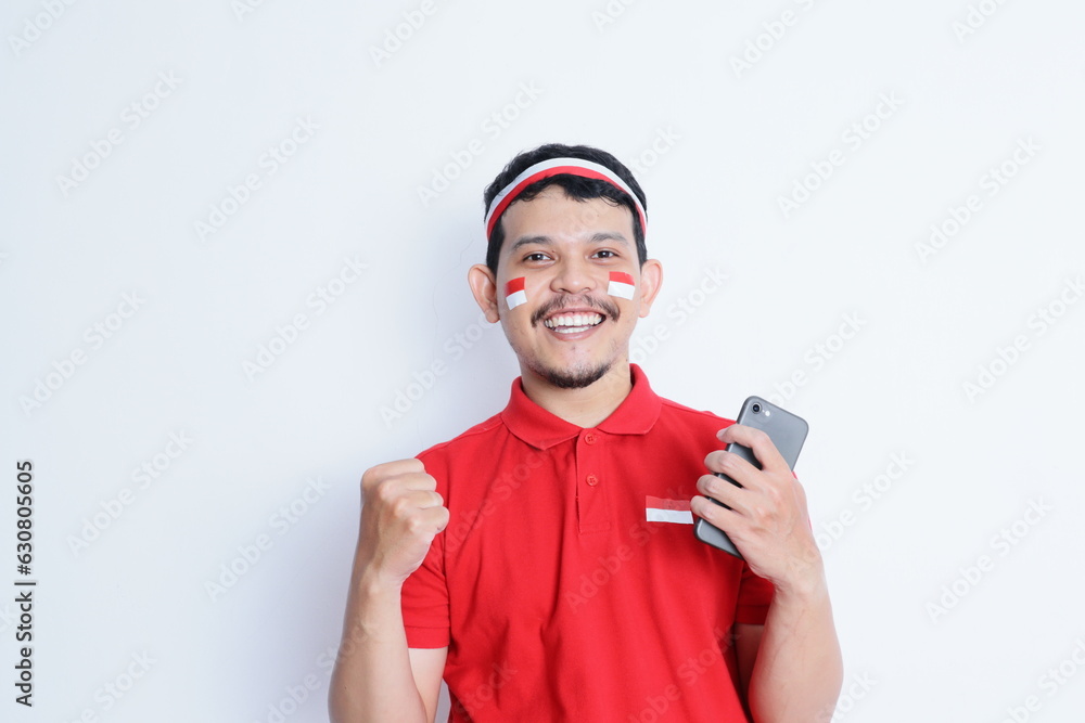 Indonesian man smiling while holding a mobile phone during independence day celebration Indonesian man smiling while holding a mobile phone during independence day celebration