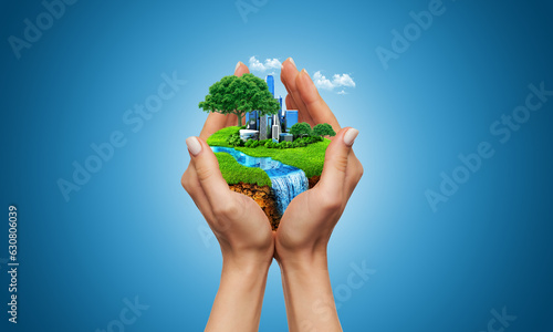 human hand holding a green landscape. human hand holding the city. hand holding green field. hand holding a city on green grass hill.