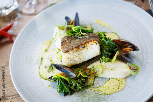 Cod fillet with cauliflower cream, asparagus, clam-wine sauce and mussles. Delicious seafood fish closeup served on a table for lunch in modern cuisine gourmet restaurant