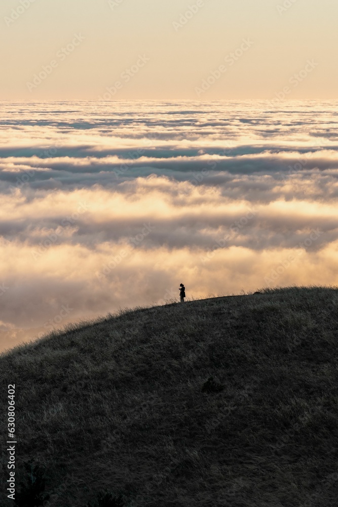 Silhouetted person standing on a hill, surveying a stunning landscape of rolling clouds