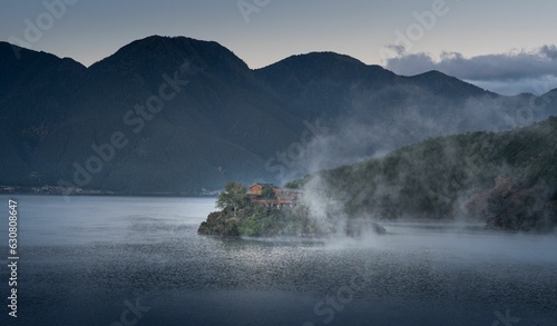 Landscape of a lake surrounded by hills covered in fog in the evening