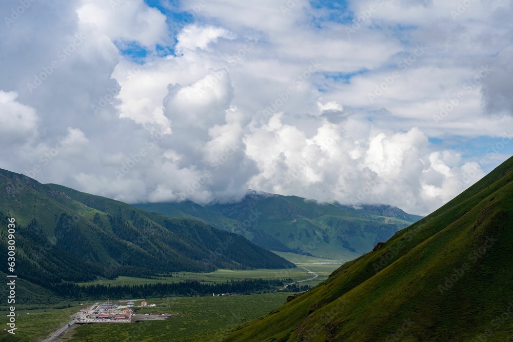 Picturesque, grassy valley surrounded by majestic, towering mountains with fluffy clouds above