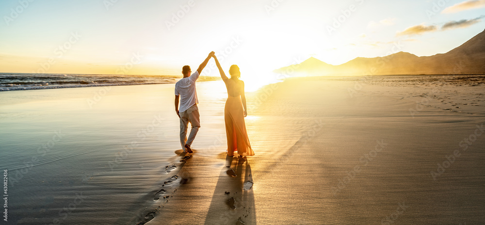Fototapeta premium Romantic couple, man and woman holding hands enjoying sea sunset on beach during travel holidays vacation. Love, getaway, honeymoon, dating.