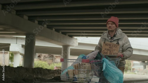 Low angle view of beggar with shopping cart going with shopping cart in unknown destination under bridge