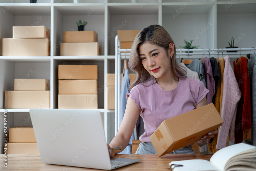 Young woman owner ship business start small business in a cardboard box and calculate price product by calculator and laptop computer Young woman owner ship business start small business in a cardboard box and calculate price product by calculator and laptop computer